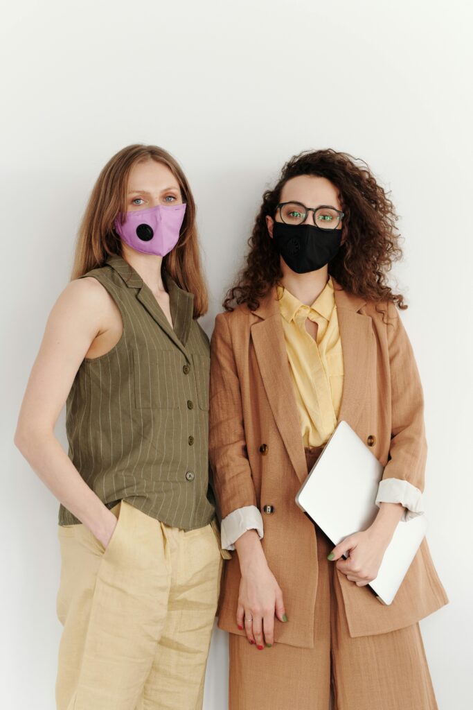Two women in professional attire wearing protective masks, promoting pandemic safety in a business setting.
