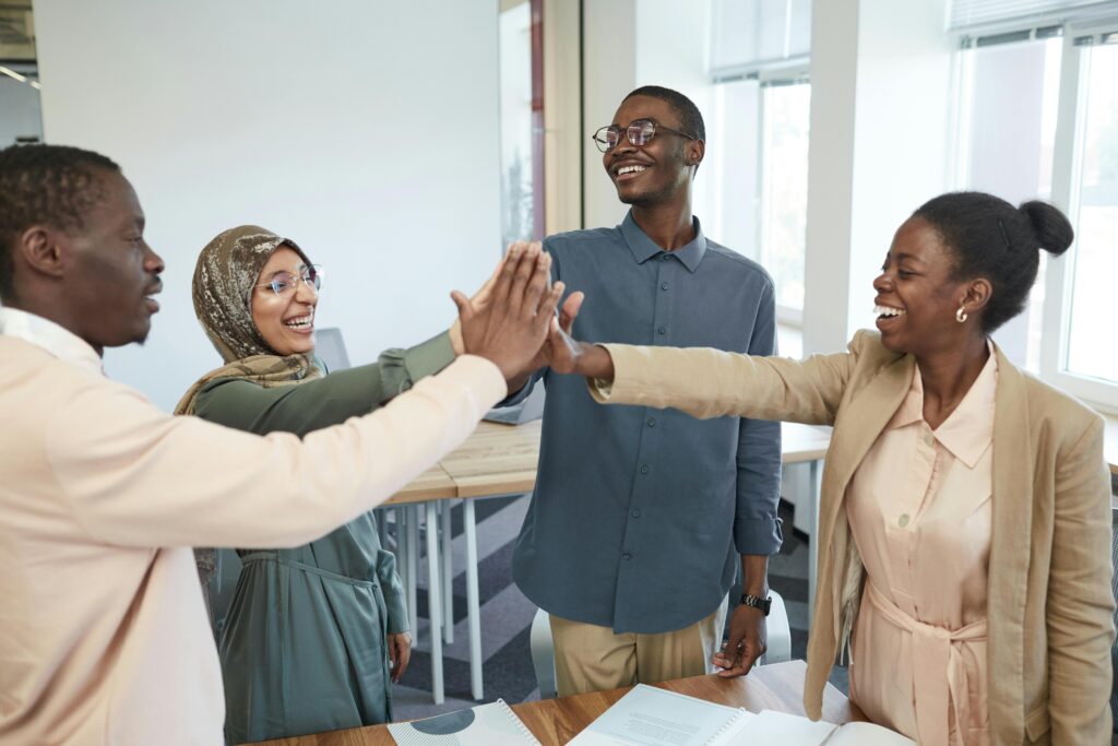A joyful group of diverse colleagues high-fiving each other in an office, symbolizing teamwork and collaboration.