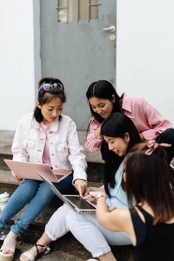 Group of young women using laptops and collaborating on outdoor stairs.
